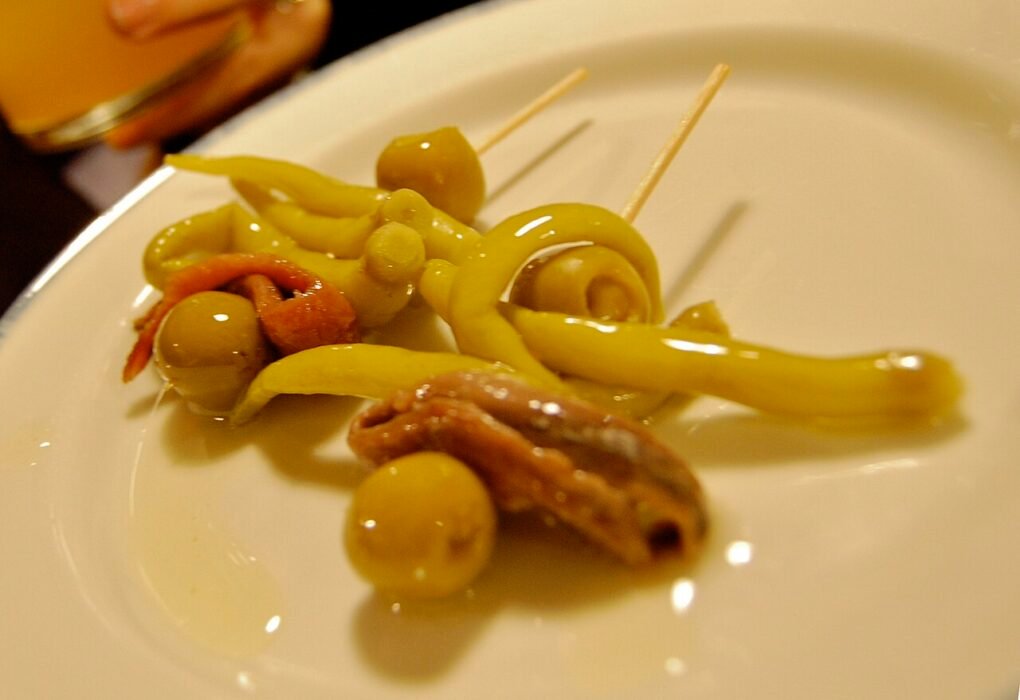 Dos gildas en un plato blanco con aceitunas, piparras y anchoas.