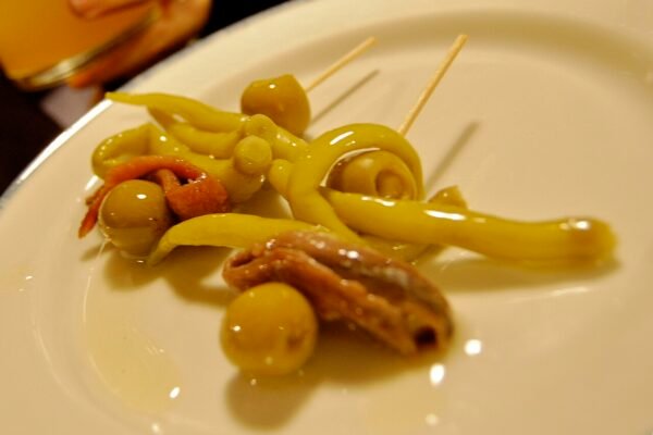 Dos gildas en un plato blanco con aceitunas, piparras y anchoas.