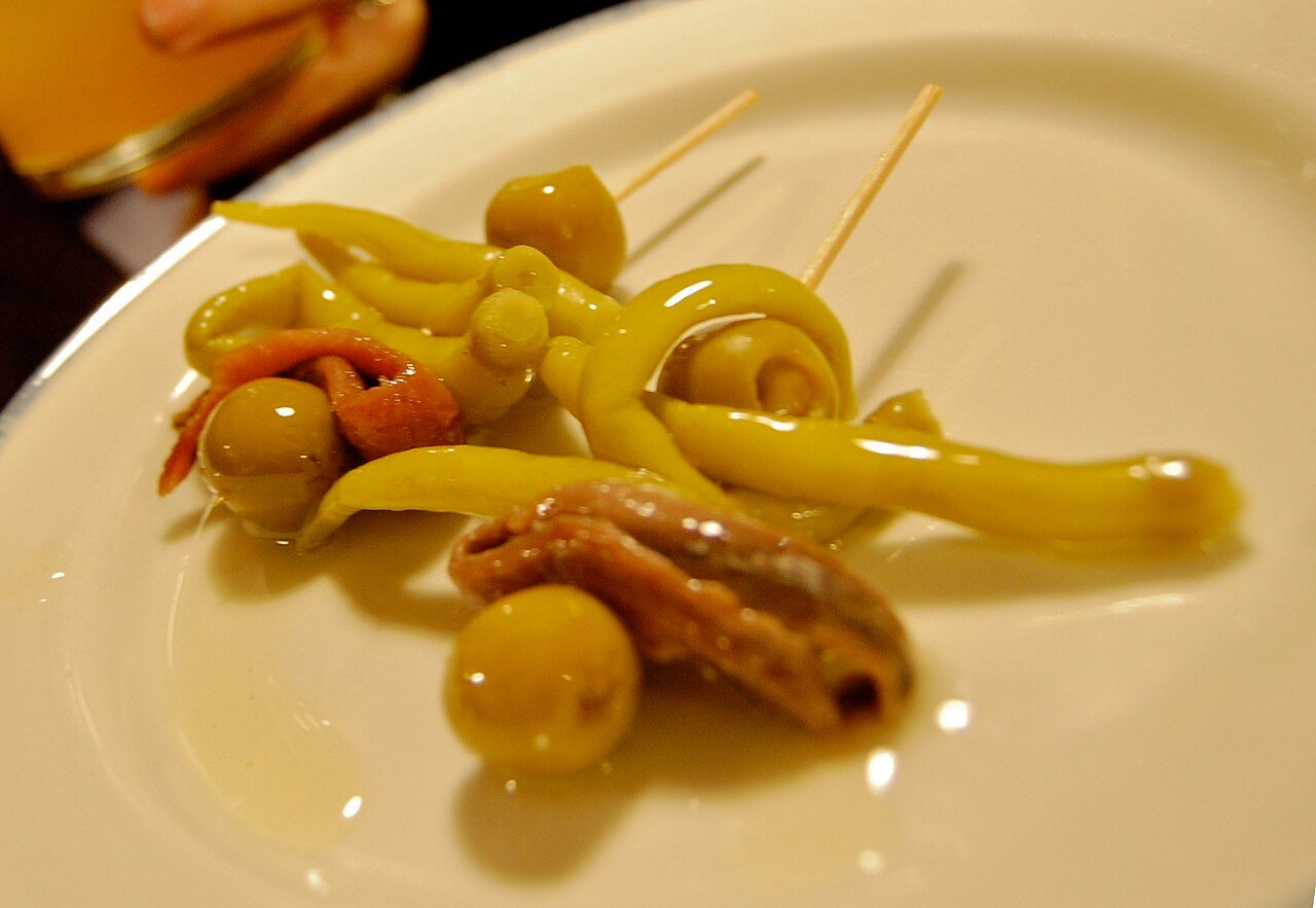 Dos gildas en un plato blanco con aceitunas, piparras y anchoas.