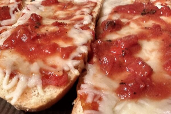 Rebanadas de pan con tomate y queso fundido en una bandeja de horno.