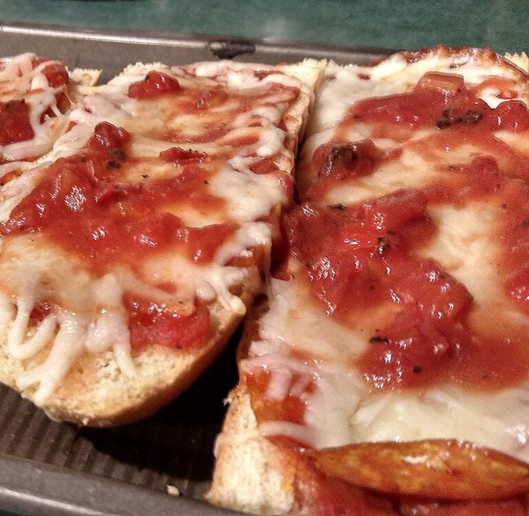 Rebanadas de pan con tomate y queso fundido en una bandeja de horno.