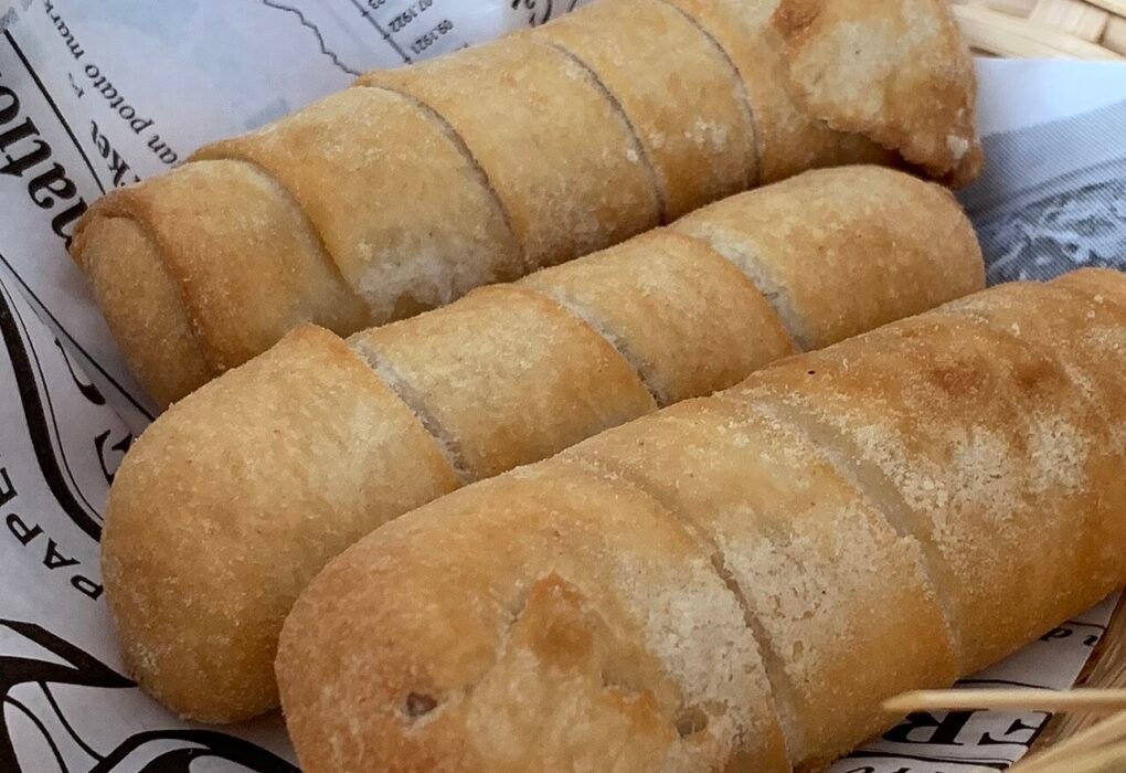 Tres tequeños fritos dorados en un recipiente con papel de estraza.