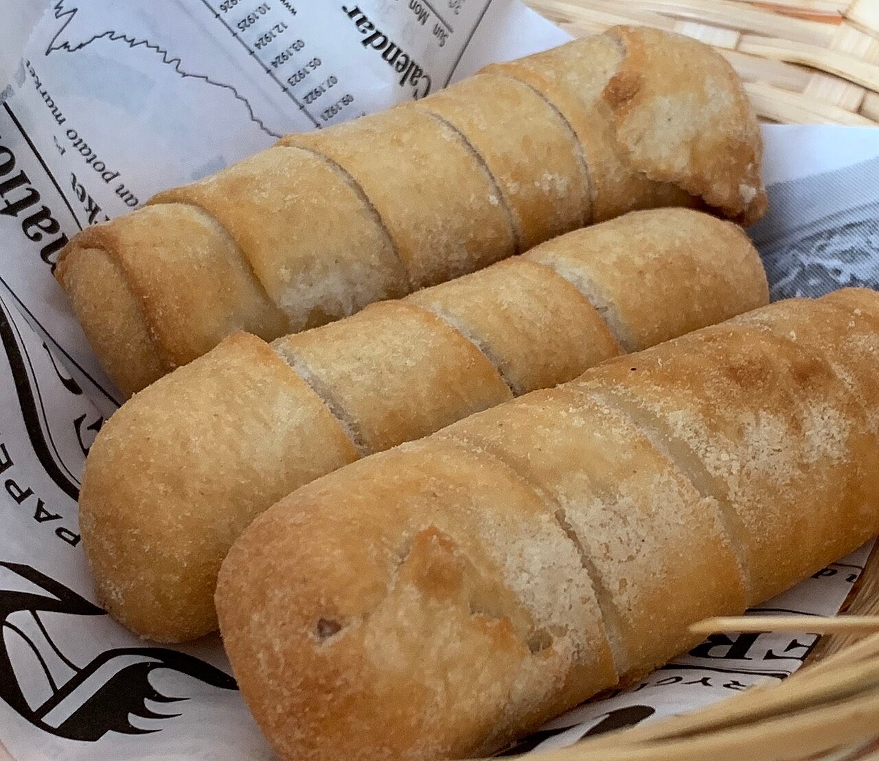 Tres tequeños fritos dorados en un recipiente con papel de estraza.