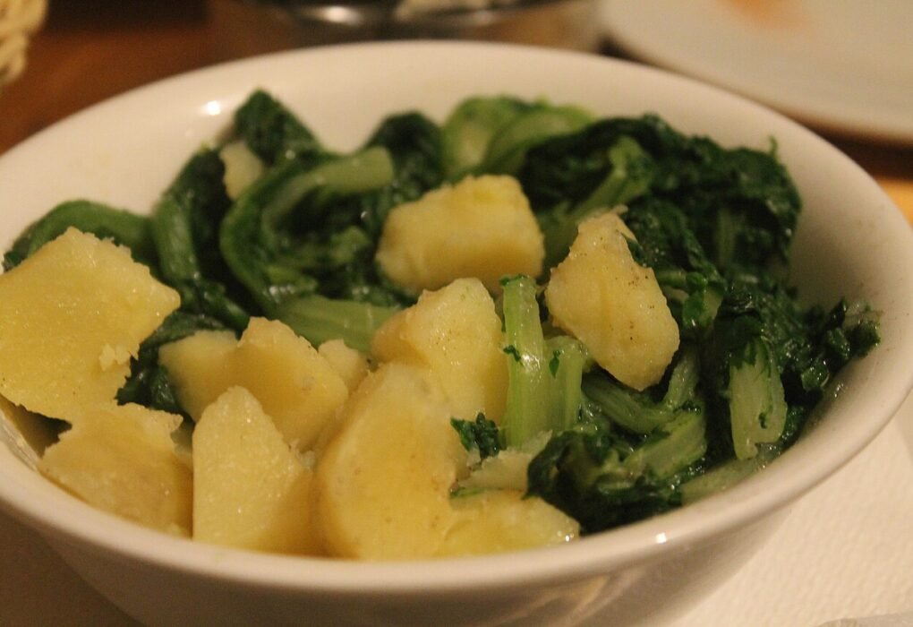 Un bol blanco con patatas cocidas y acelgas verdes.