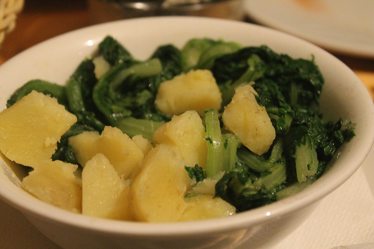 Un bol blanco con patatas cocidas y acelgas verdes.