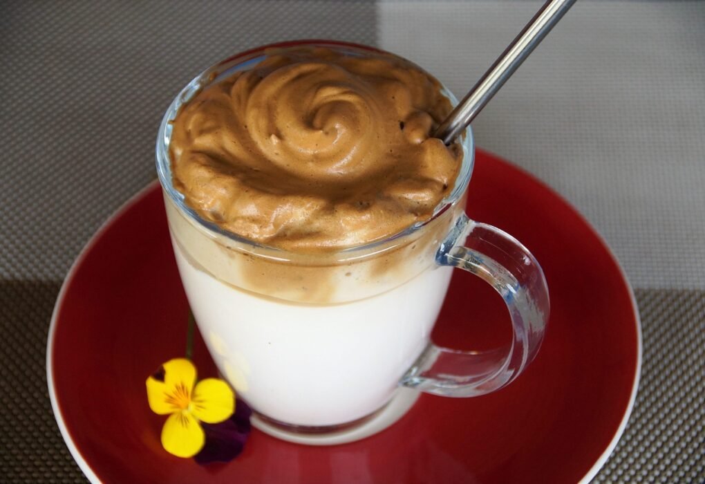 Un vaso de cristal con leche y una gruesa capa de crema de café dalgona encima, sobre un plato rojo.